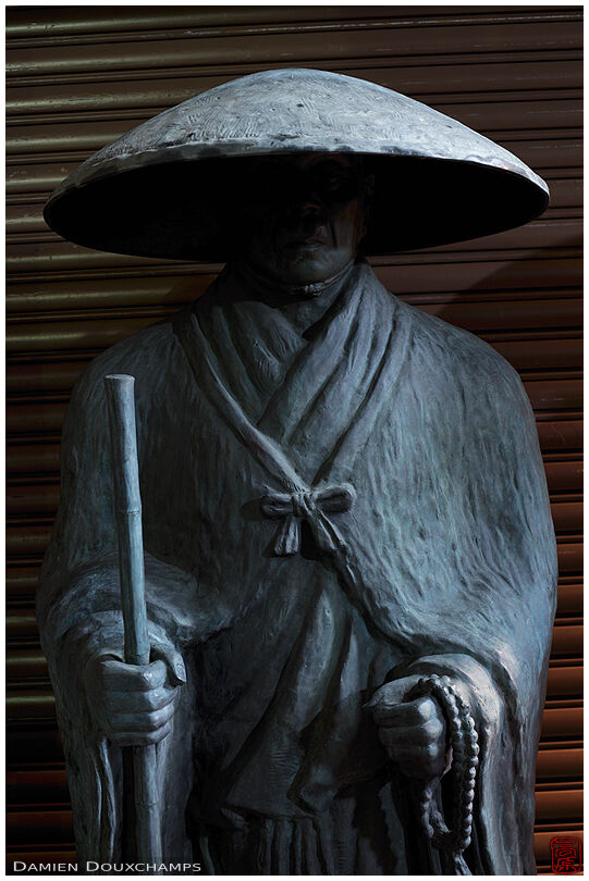 Pilgrim statue in front of store shutters, Kyoto, Japan