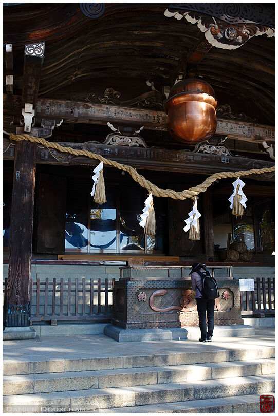 Praying under the massive bell and rope of a temple at the foot of Mt Tsukuba, Japan