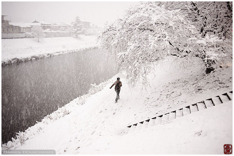 Man waling fast along the Takano river during a snow storm in Kyoto, Japan