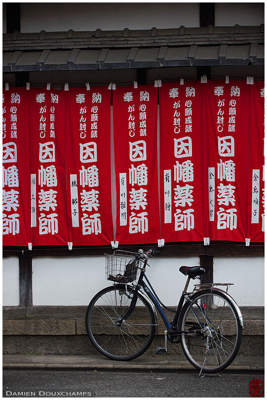Bicycle parked under red flags at the entrance of Byodo-ji temple, Kyoto, Japan