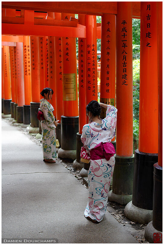 Two girls in kimono under the red torii gates of Fushimi Inari shrine, Kyoto, Japan
