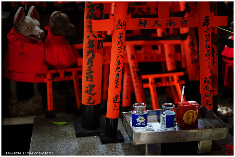 Sake cups and small red torii gates as offerings in a small shrine on the mountains of Fushimi Inari Taisha, Kyoto, Japan