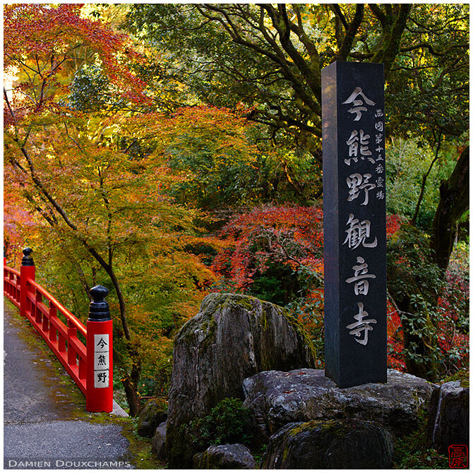 The entrance of Imakumano Kannon-ji temple with its large stone marker and traditional red bridge, Kyoto, Japan