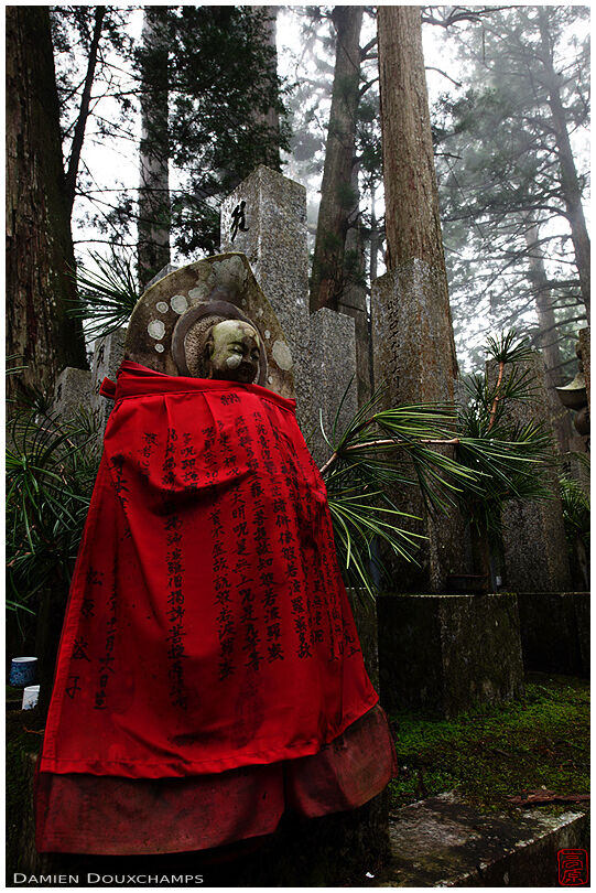A jizo statue with a red bib in the foggy forest of Okunoin, the cemetery of Koyasan in Wakayama, Japan