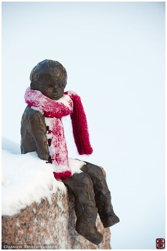 Snow-covered little boy statue with red scarf
