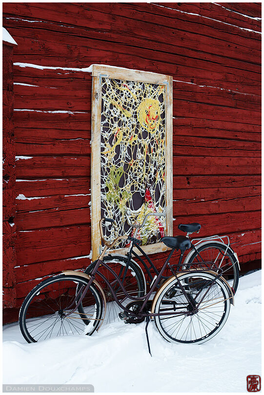 Two bicycles in the snow under a rope art panel on an old wooden house of Oulu harbour, Finland