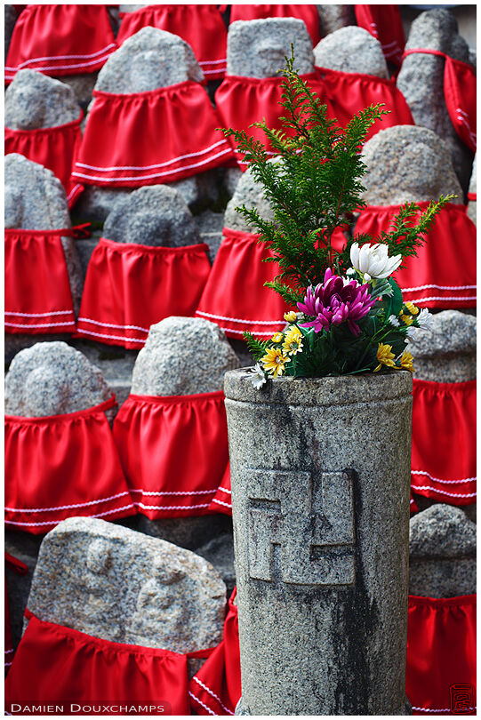 Flowers in front of a mountain of jizo statues with red bibs, Rokuhara Mitsui temple, Kyoto, Japan