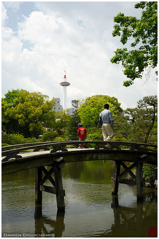 Father and kid on old bridge with Kyoto Tower in background, Shosei-en park