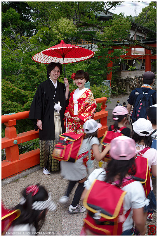 Couple in full wedding attire being photo-bombed by a group of school kids near Uji shrine, Kyoto, Japan