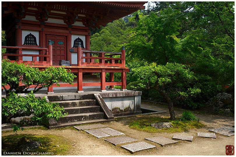 Small red pagoda amidst green vegetation, Mimuroto-ji temple, Kyoto, Japan