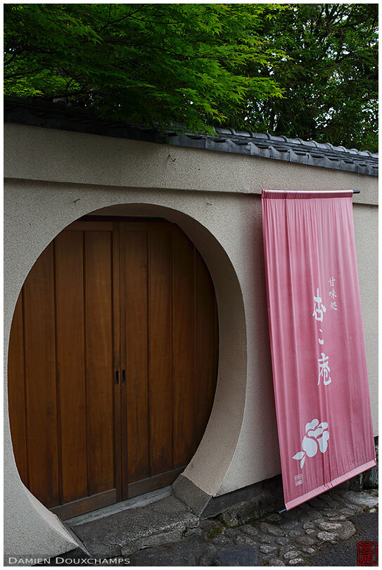 Round entrance door of a shop with pink sign in the Nanzenji temple complex, Kyoto, Japan