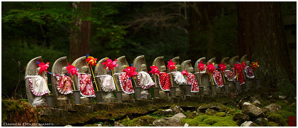 A row of jizo statues with bib and little wind mills in the forest of Kongorin-ji temple, Kyoto, Japan