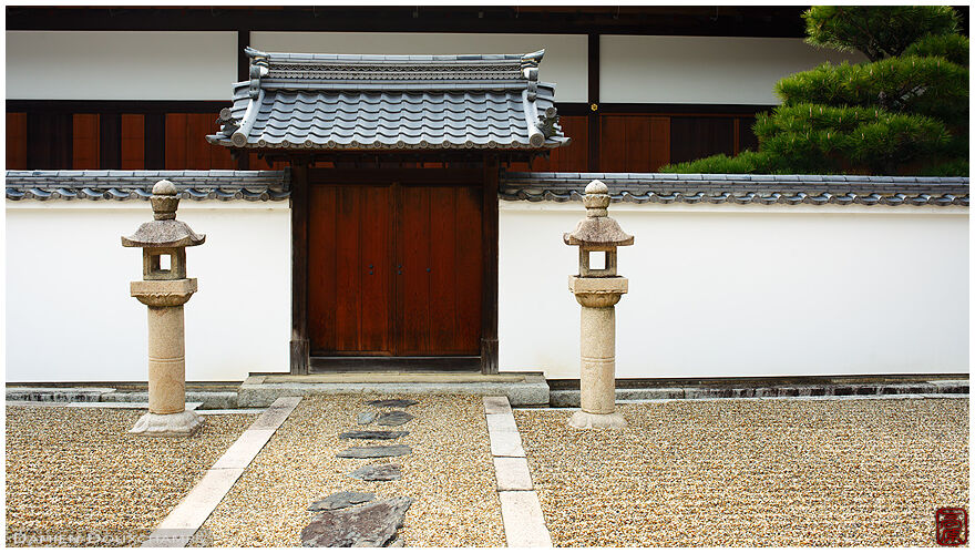 Raked gravel grounds and two stone lanterns in front of the gate to a subtemple of Manpukuji, Kyoto, Japan