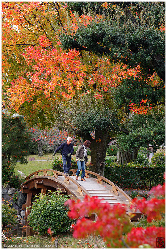 Visitors on a curved wooden bridge in the Shosei-en garden, Kyoto, Japan