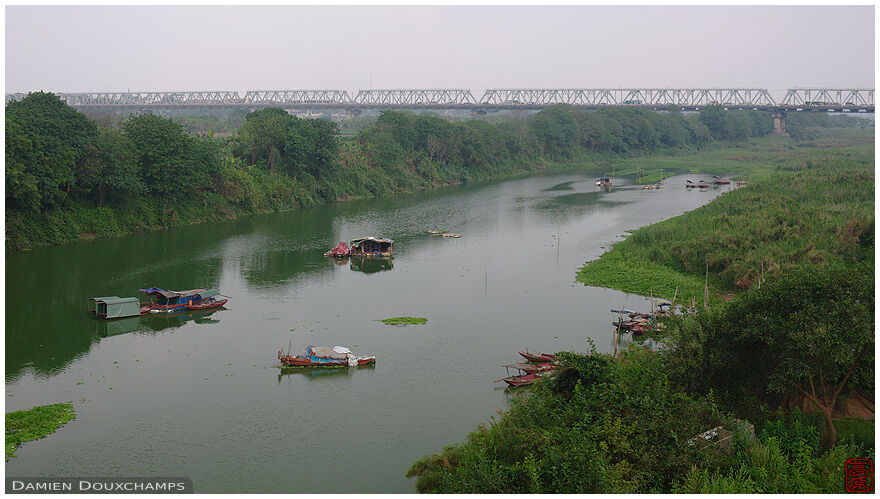 Boats and floating houses on Hanoi Red River with the Cầu Chương Dương bridge in the background, Viet Nam