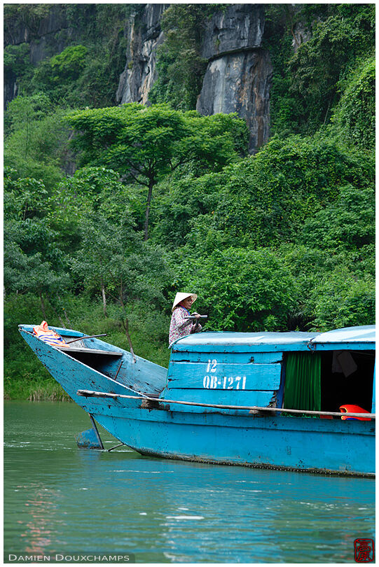 Old lady driving blue tourist boat at the entrance of the Phong Nha cave, Viet Nam