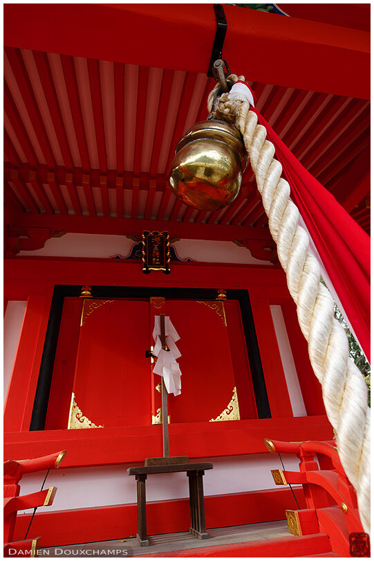 Golden bell and bright red shrine in Kitano Tenmangu, Kyoto, Japan