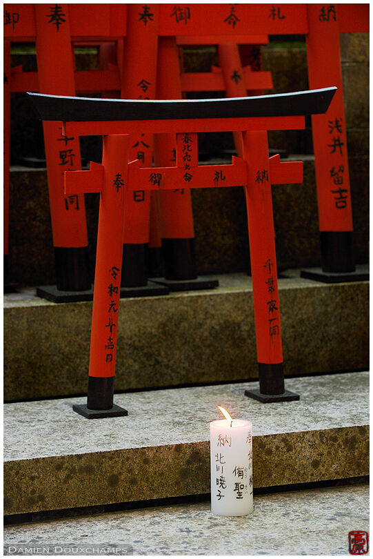 Candle burning in front of small torii votive offerings in the local Goshanotaki shrine, Kyoto, Japan