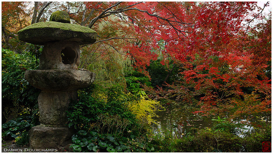 Massive and old stone lantern amidst autumn foliage in Okazaki Betsuin temple, Kyoto, Japan