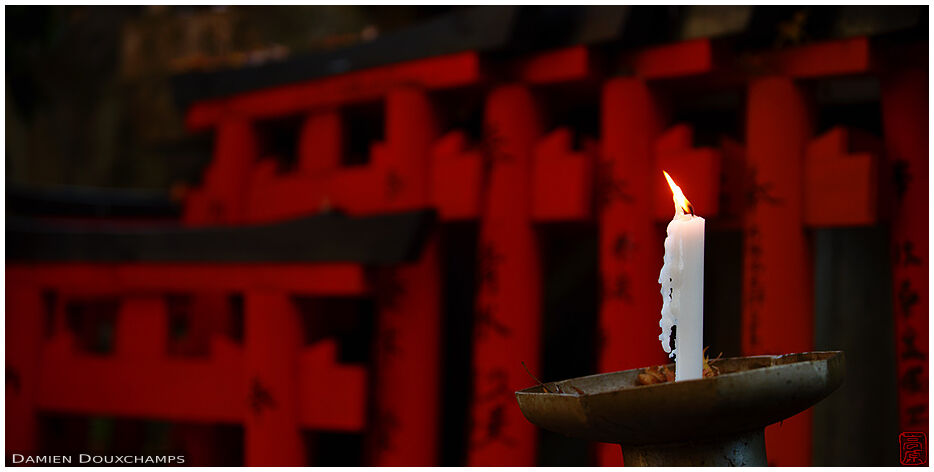 Candle burning in front of torii in dark corner of Goshanotaki shrine, Kyoto, Japan
