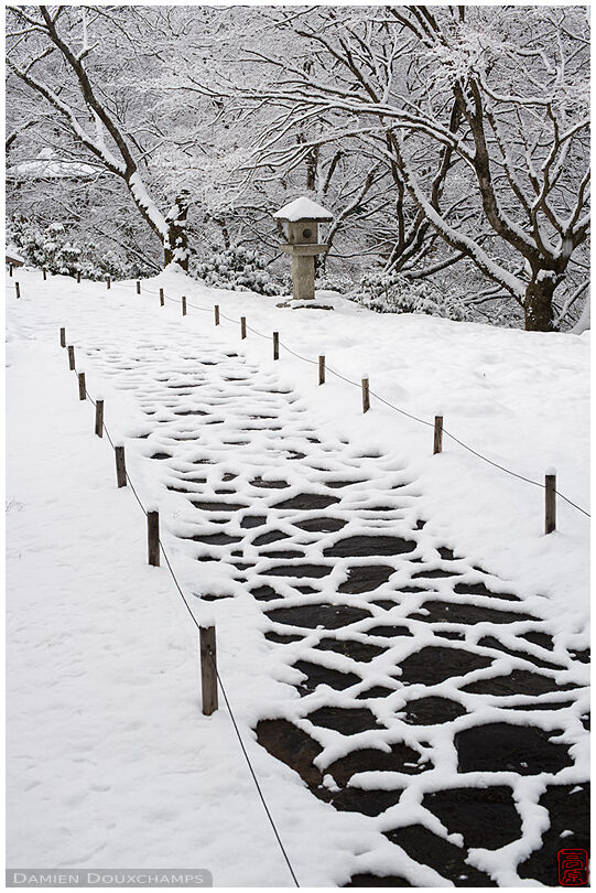 Stone path and lantern in the winter wonderland of Hakuryu-en garden, Kyoto, Japan