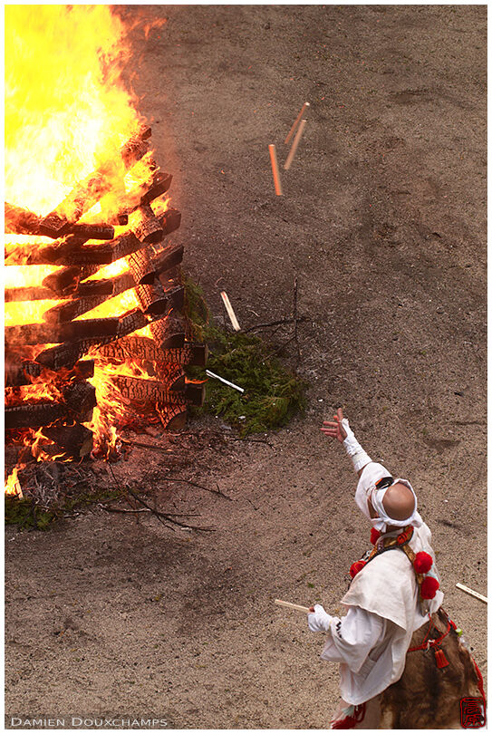 Monk throwing votive offerings pine tablets in large fire during festival in Tanukidani-san Fudoin temple, Kyoto, Japan
