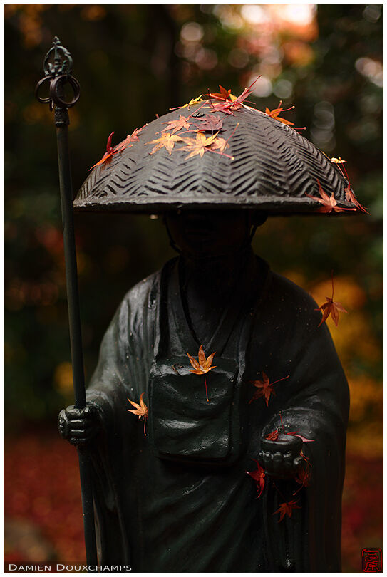 Pilgrim statue covered with fallen maple leaves, Konzo-ji temple, Kyoto, Japan