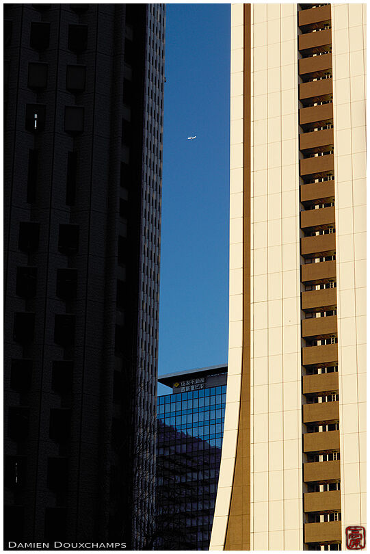 Airplane passing between tall buildings in the business district of Shinjuku, Tokyo, Japan